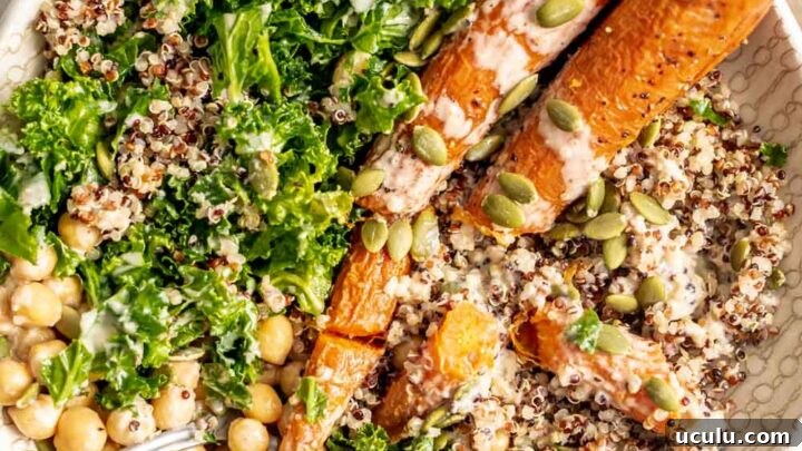 Roasted carrots, kale, quinoa, chickpeas and pumpkin seeds in a bowl topped with tahini sauce.