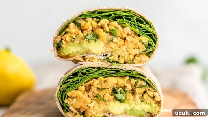 Two stacked halves of a chickpea salad, avocado and spinach wrap cut on a cutting board.
