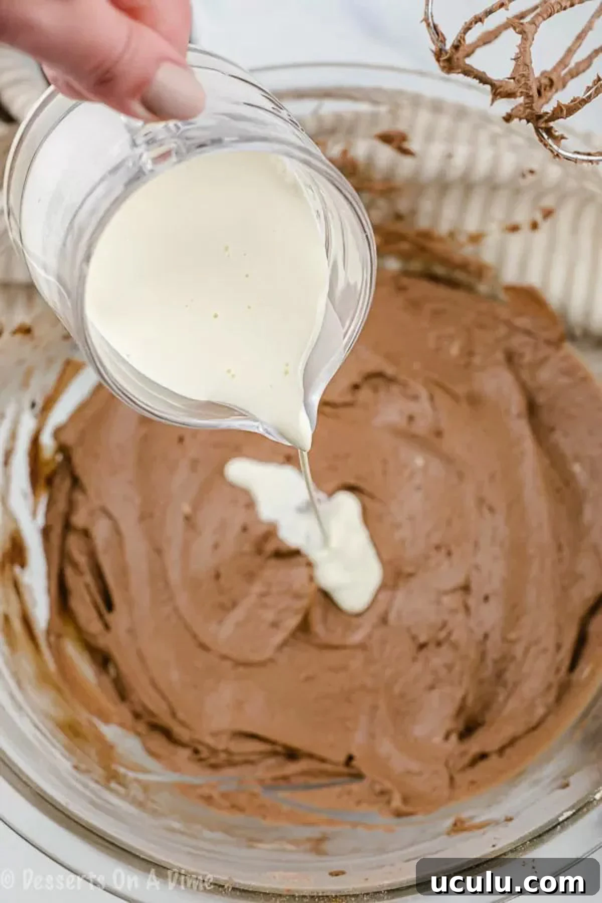 The process of pouring heavy cream in the chocolate frosting.