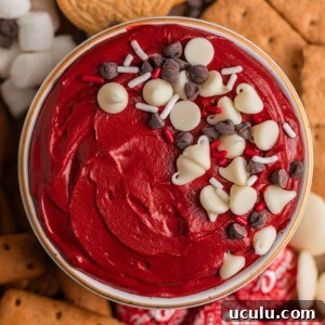 Overhead view of red velvet cake dip in bowl with sprinkles and chocolate chips over top.