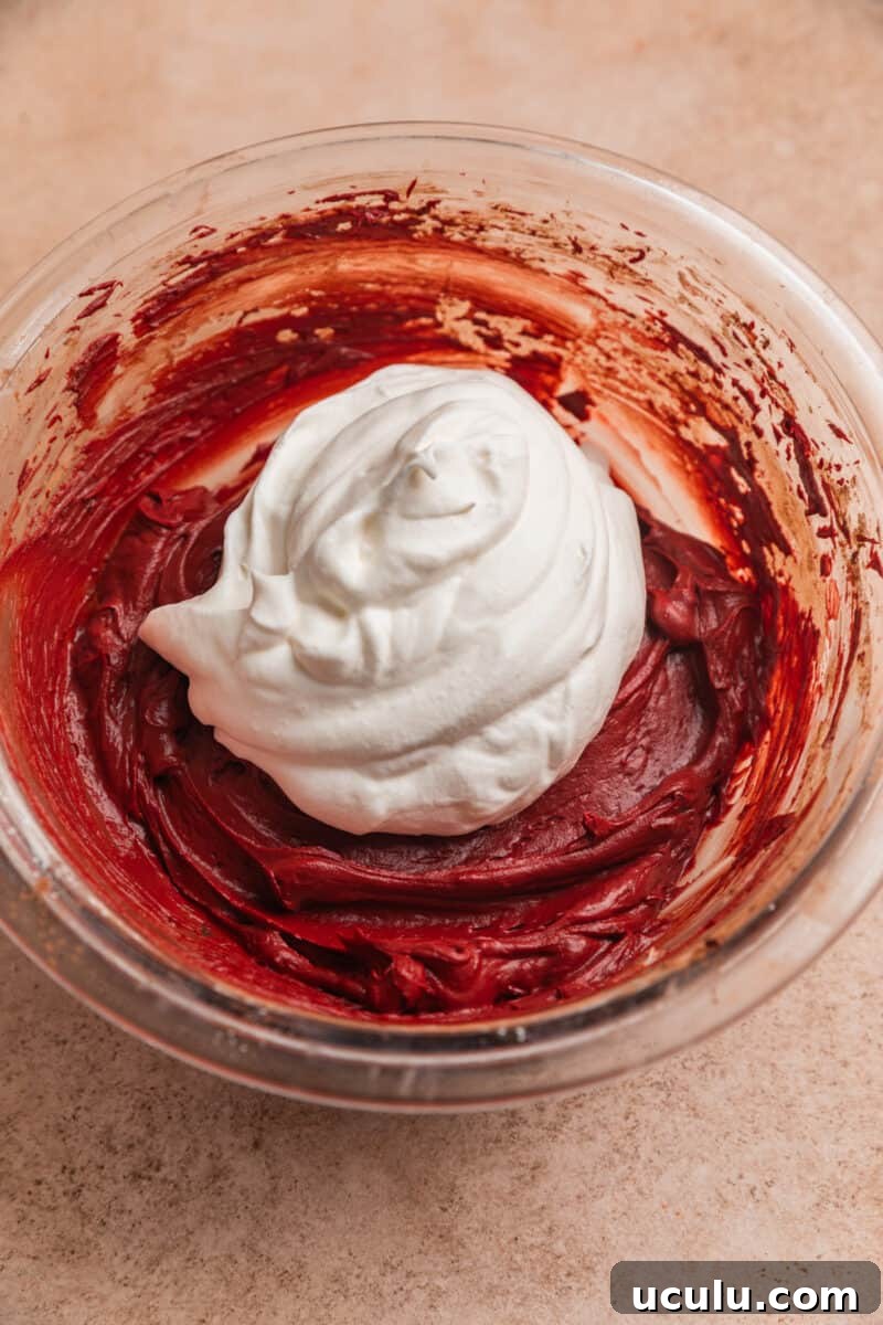 Whipped cream on top of red velvet cheesecake dip in glass bowl.