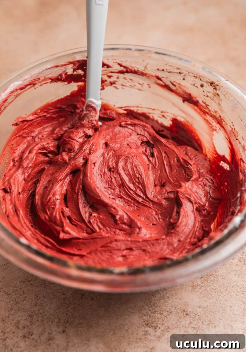 Red velvet dip in mixing bowl with white spoon.