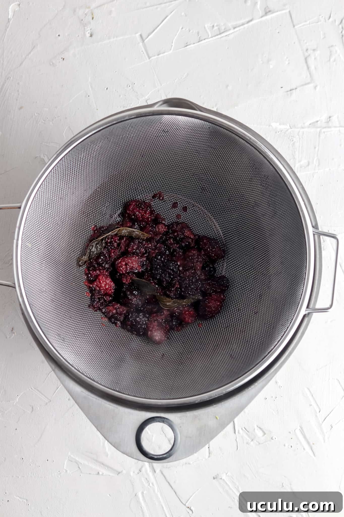 Simple syrup being strained over a metal strainer.