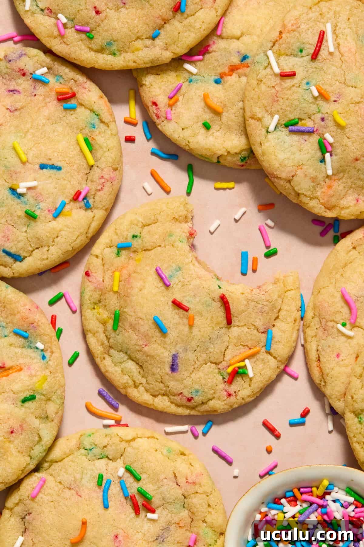 Funfetti birthday cake cookies arranged on surface with bite taken out of one cookie.