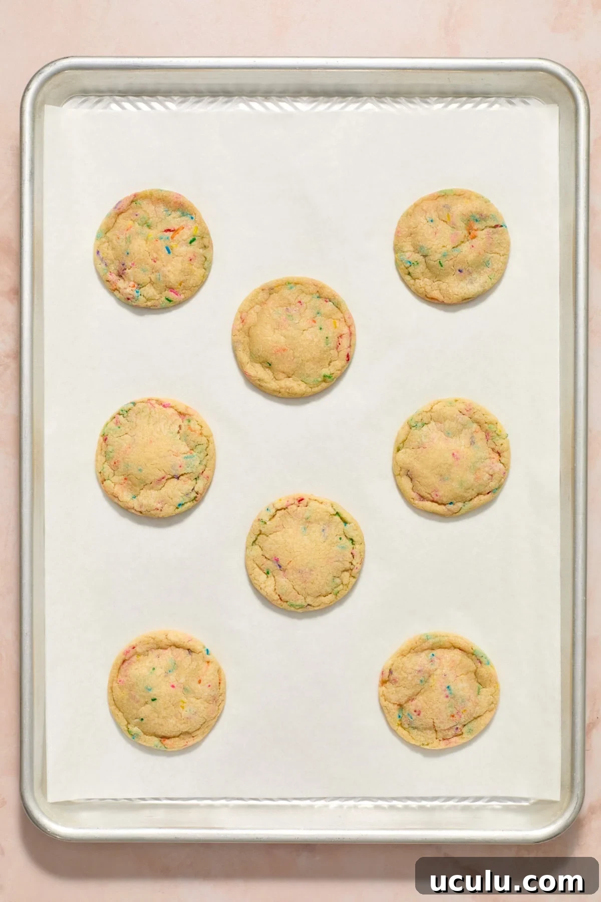 Baked birthday cake cookies on parchment paper lined cookie sheet.