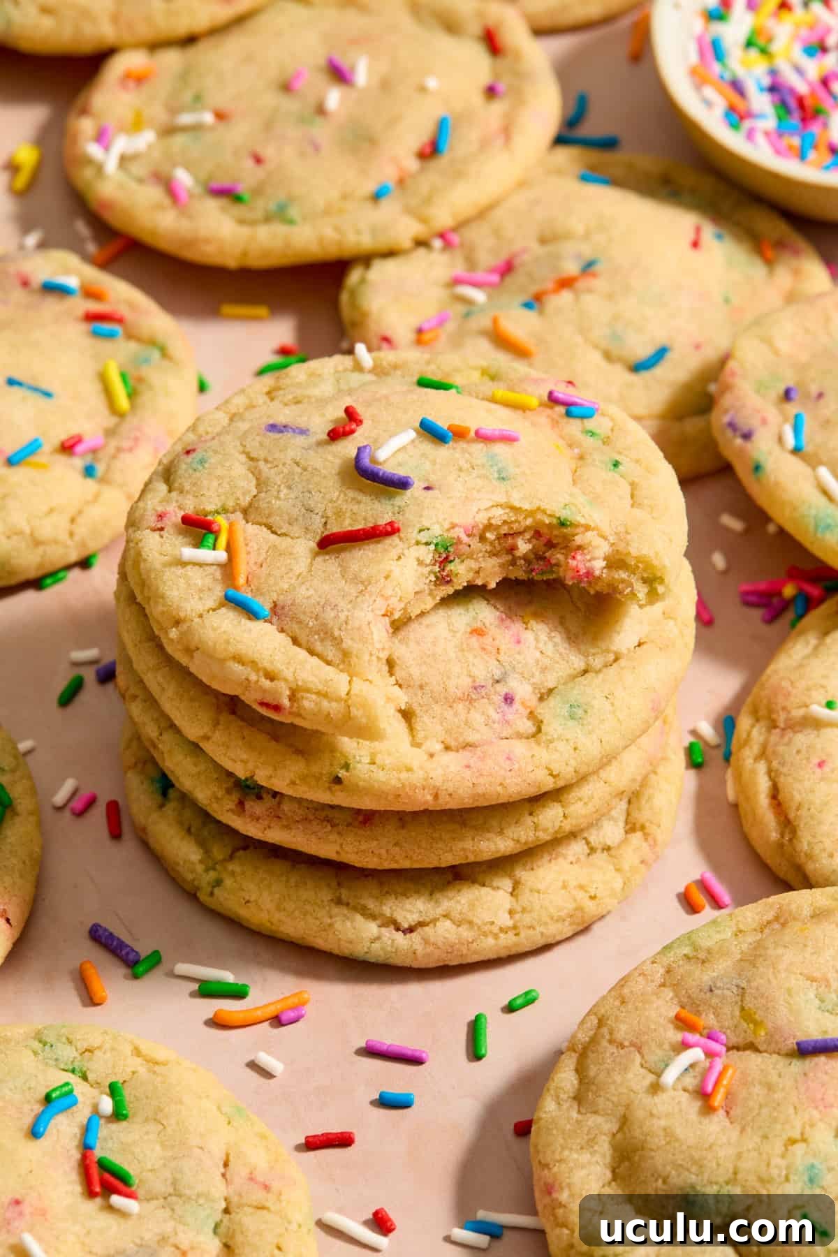 Stack of birthday cake cookies with rainbow sprinkles and bite taken out of top cookie.