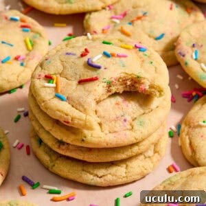 Stack of funfetti rainbow sprinkle filled cookies with bite taken from the cookie on top of stack.