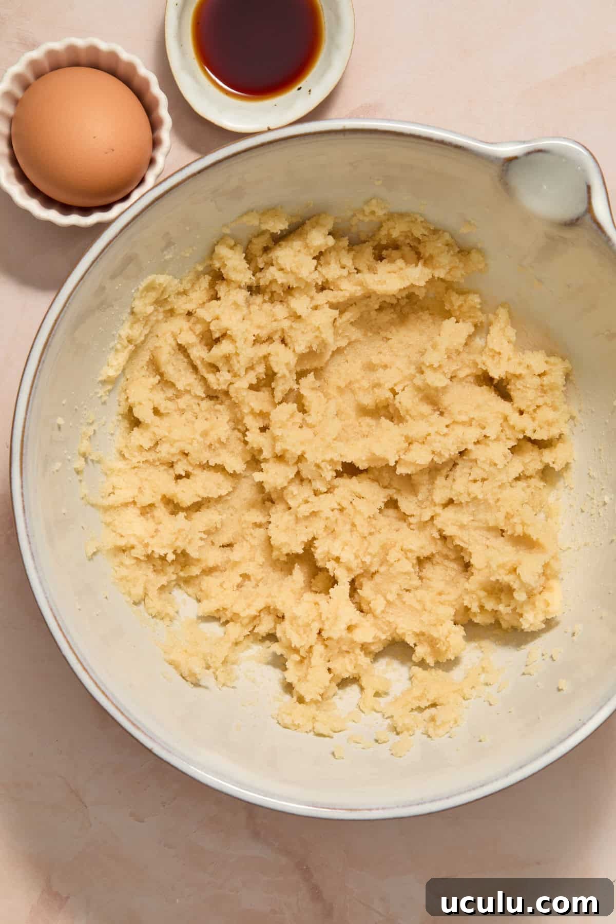 Butter and sugars creamed in mixing bowl with vanilla extract and egg beside bowl