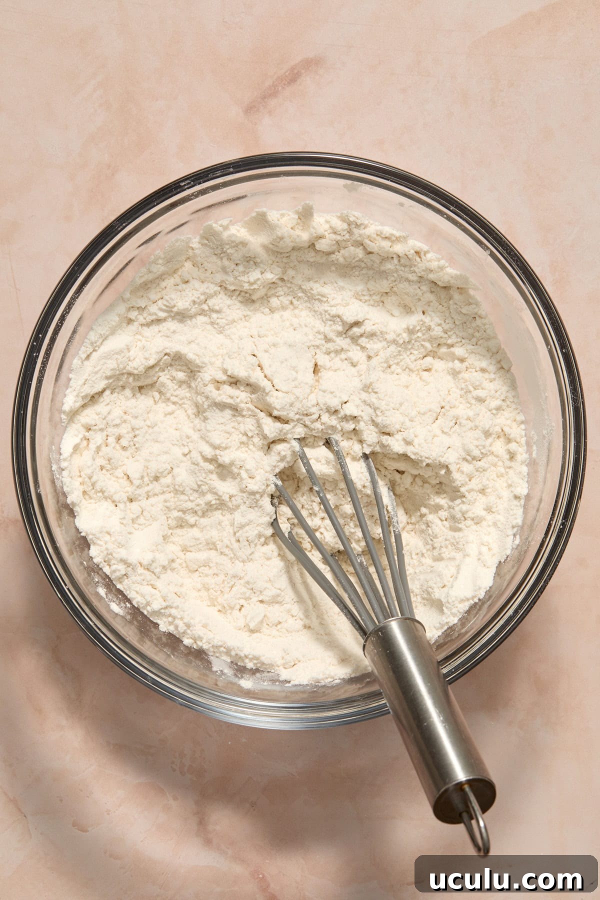 Dry ingredients in glass bowl with whisk.