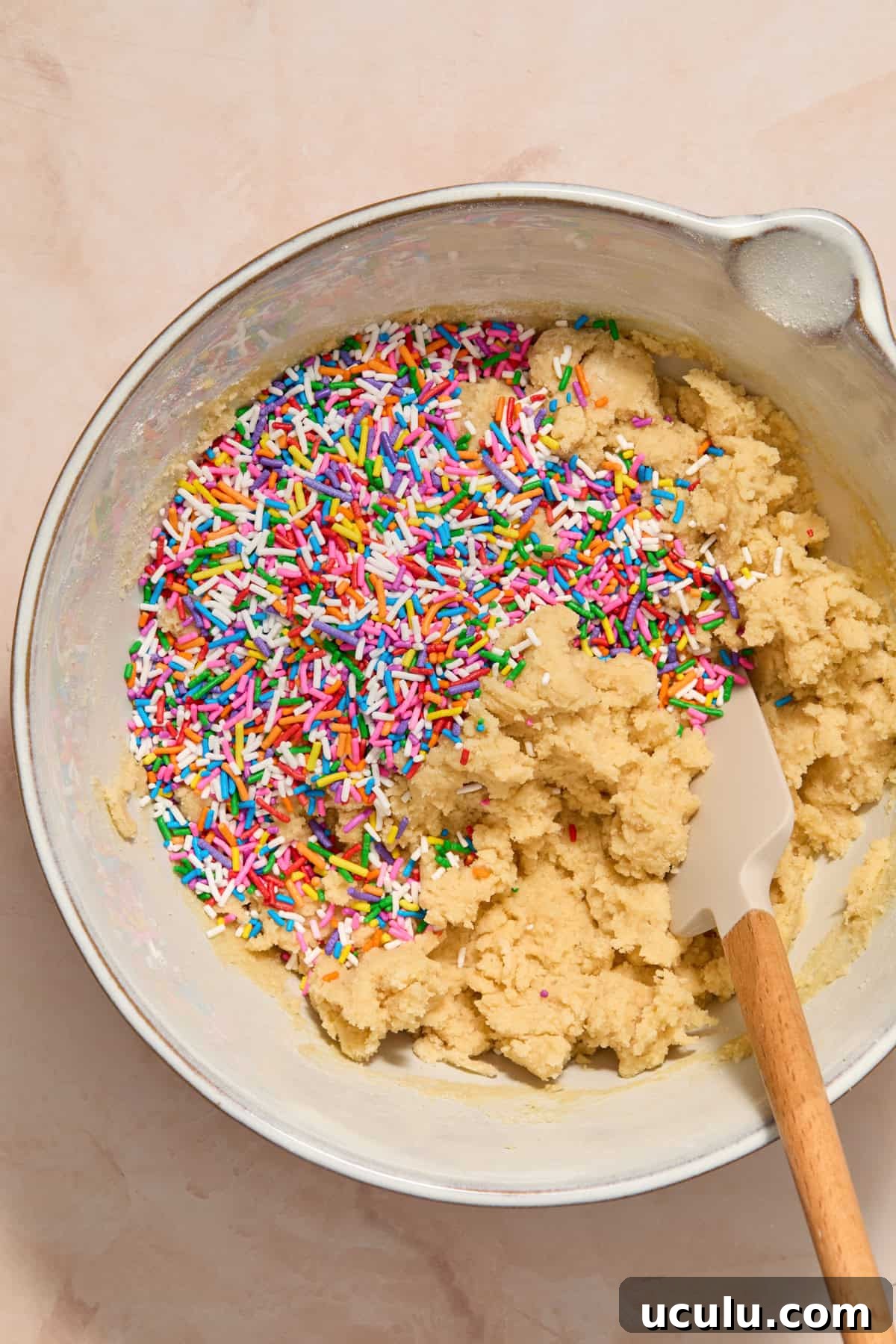 Rainbow sprinkles poured into bowl with birthday cake cookie dough mixture.