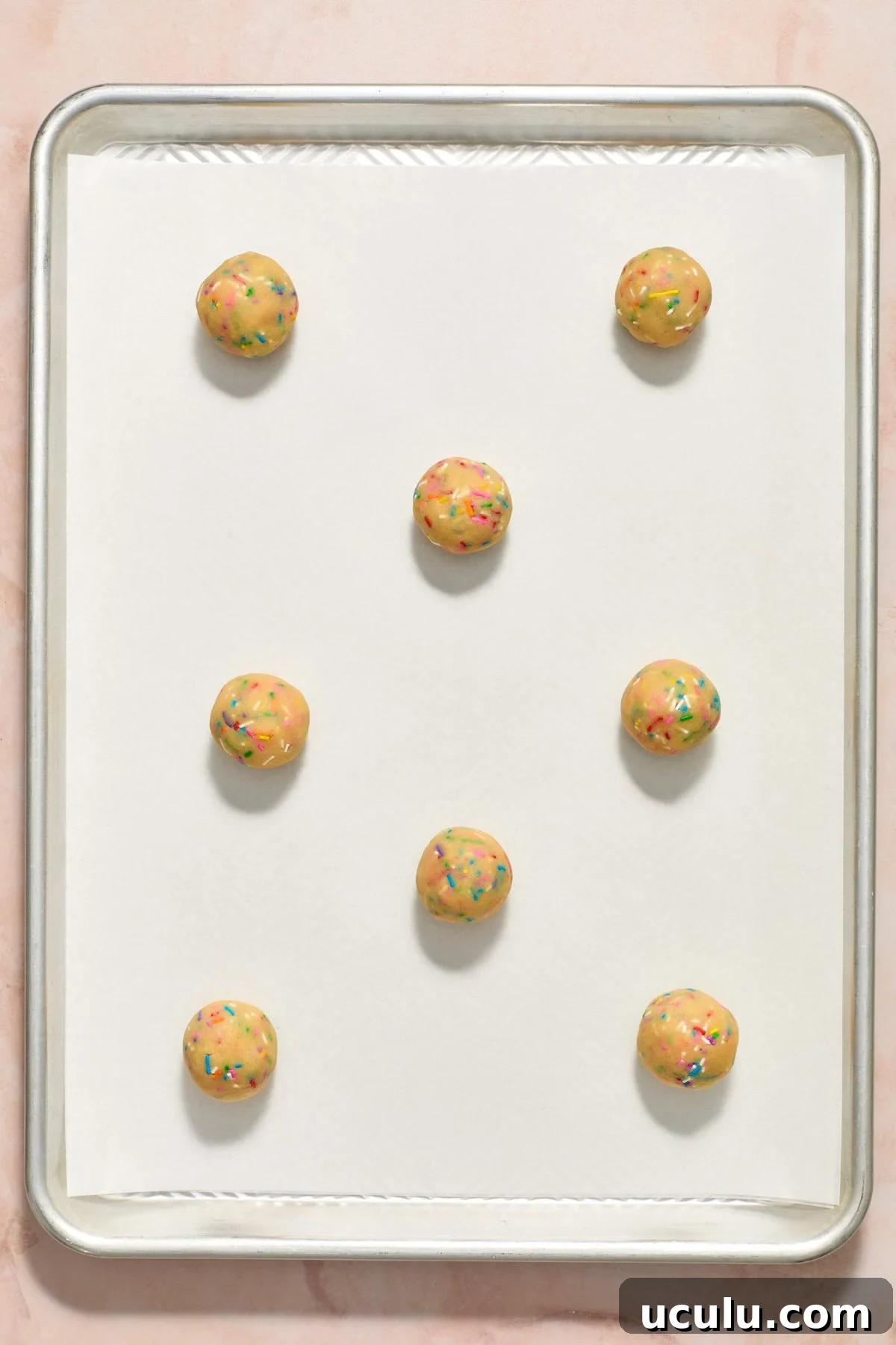 Birthday cake cookie balls on parchment paper lined cookie sheet before baking.