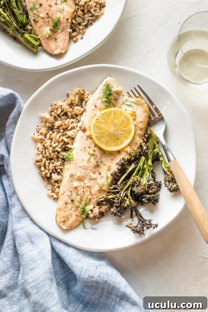 Rainbow trout baked with lemon and garlic and served on a small white plate along with roasted broccolini and a wild and brown rice mix.
