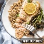 Close up of baked rainbow trout served on a plate, being flaked with a table fork.