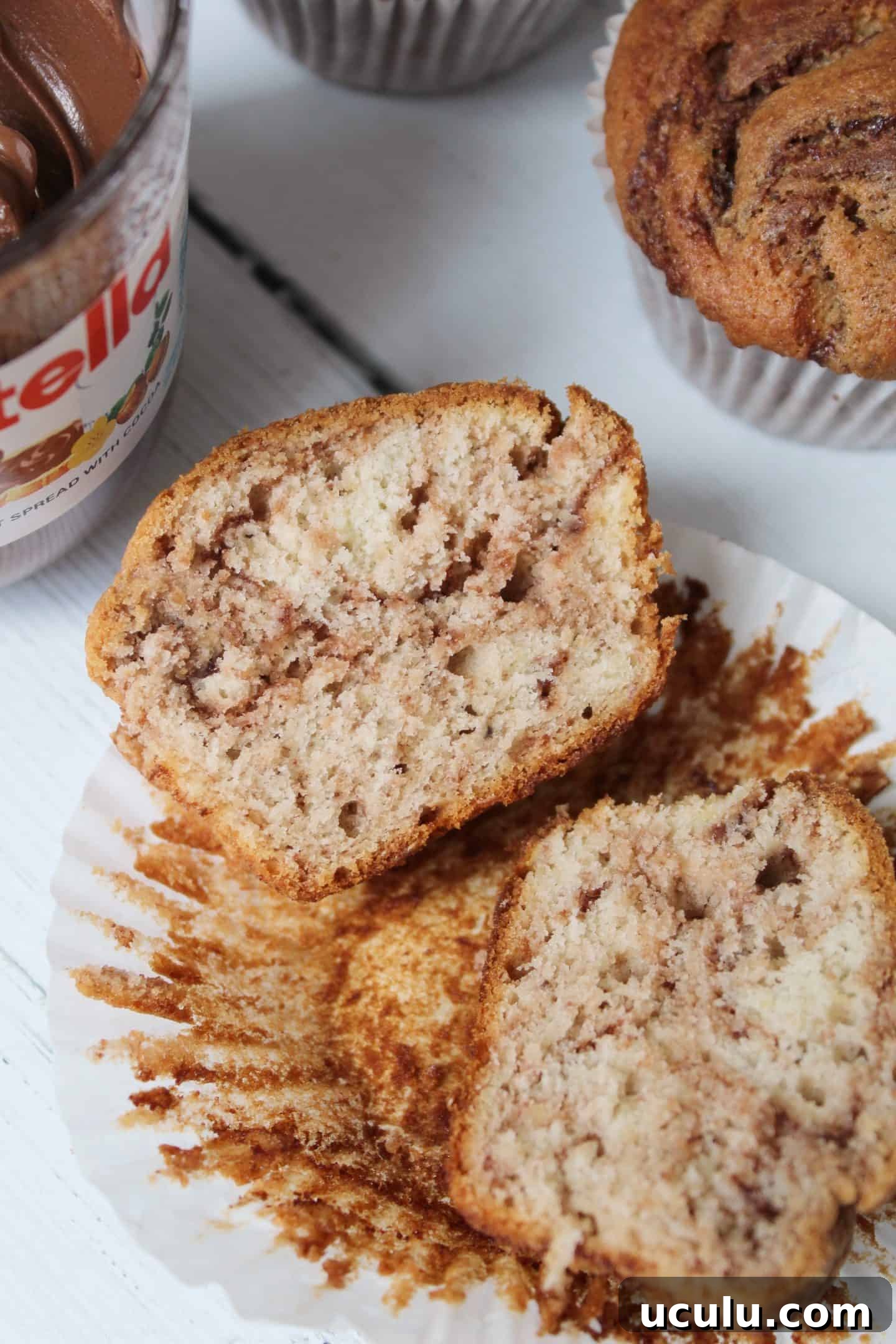 Gluten free banana nutella muffins on a white wooden worktop with a jar of Nutella in the background.