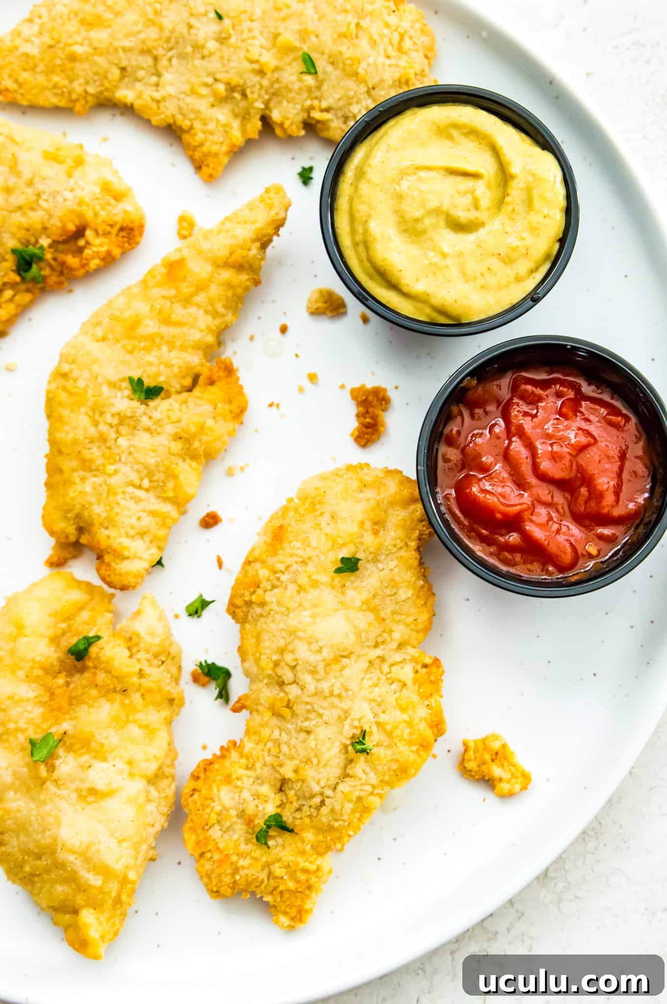 A plate of cooked chicken tenders with a side of ketchup and mustard.