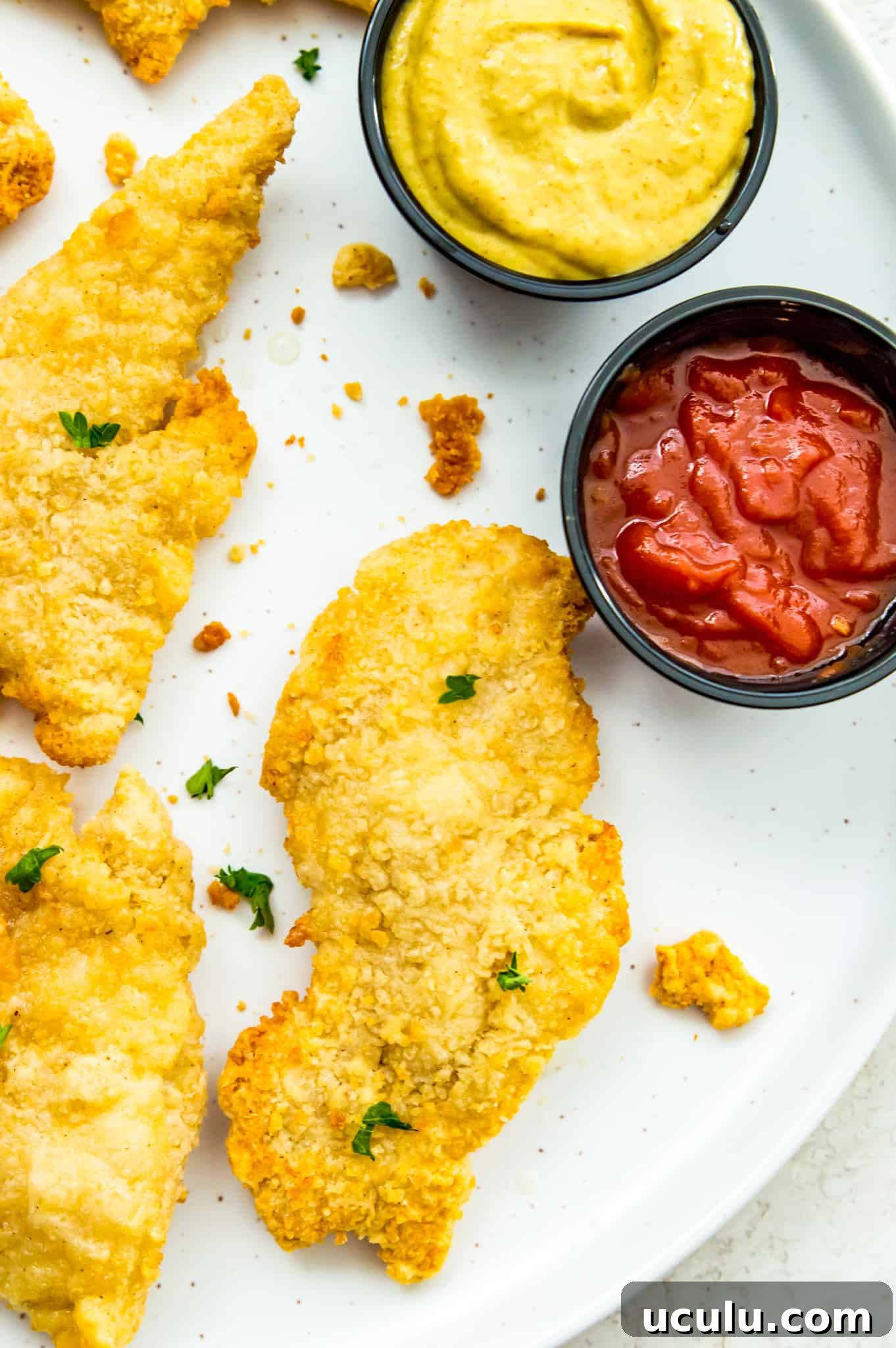 A plate of cooked chicken tenders with a dish of ketchup beside them.