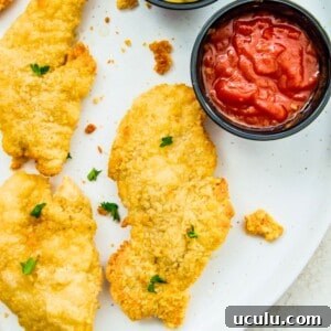 Cooked chicken tenders on a plate with a dish full of ketchup beside them.