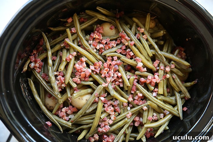 A slow cooker filled with baby potatoes, green beans, and cubed bacon pieces.