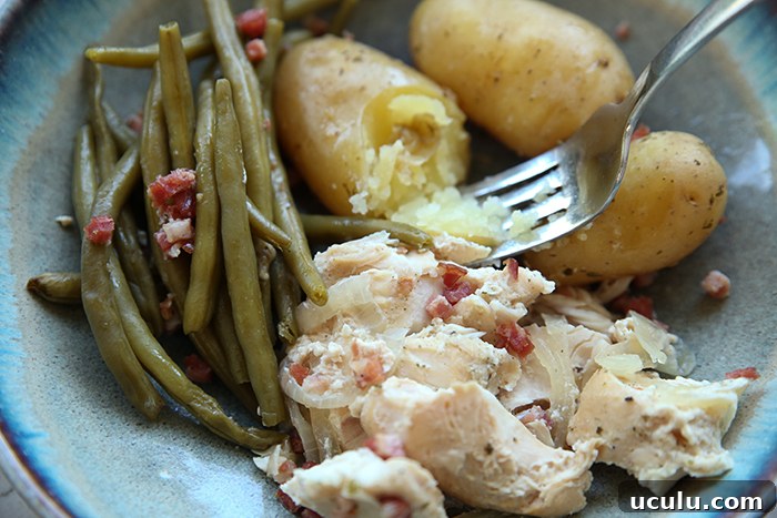 A serving of green beans and chicken with bacon bits and three small potatoes with a fork that has the edge of a potato mashed on it.