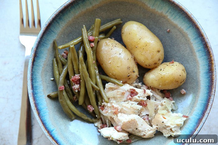 A dinner bowl plate with three small whole potatoes, green beans with bacon, and chicken with onions and bacon bits with a fork on the left.