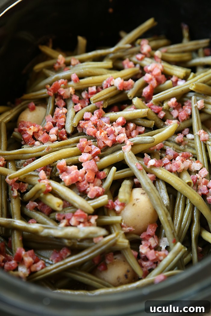 A crockpot with small whole potatoes, green beans, and cubed bacon bits.
