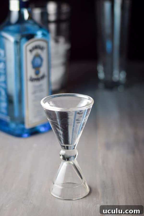 Gin poured out with the bottle, shaker and glass in the background