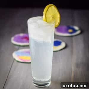 A tall flared glass filled with the collins. There is a lemon wheel on the rim - Square