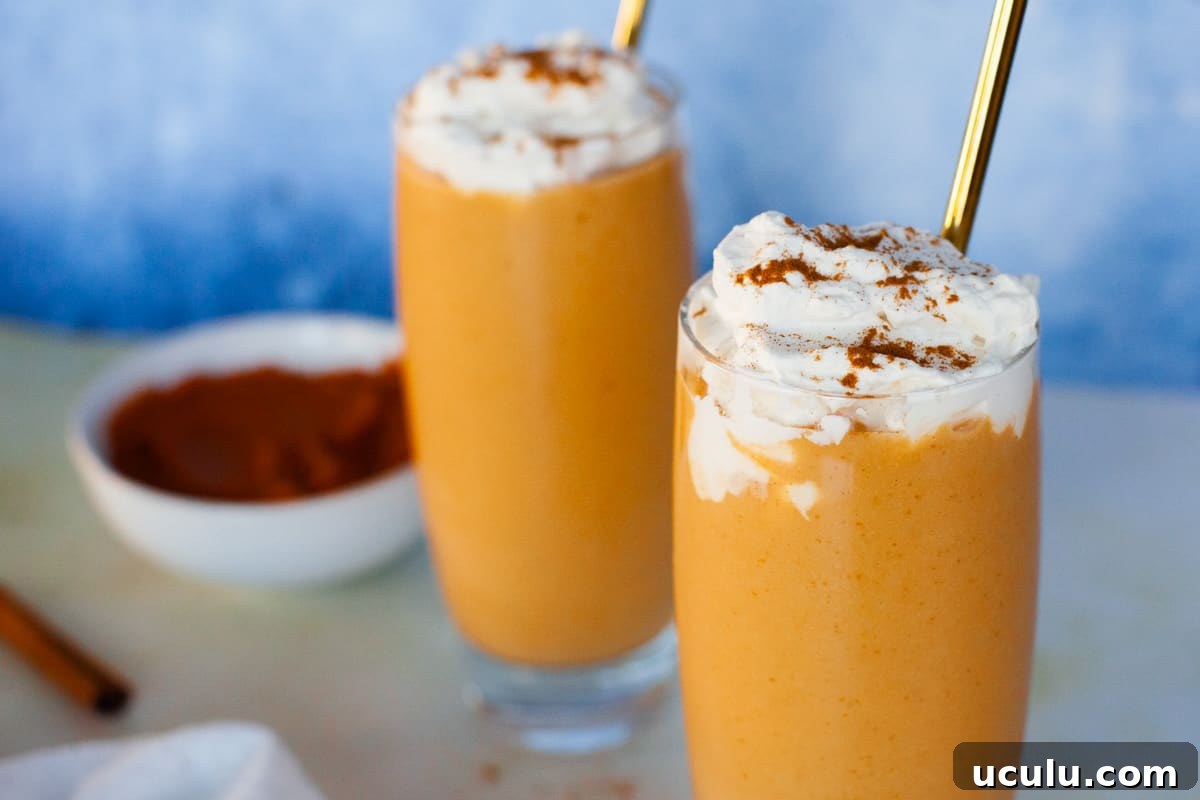 Two pumpkin smoothies topped with cinnamon sprinkled whipped cream and gold straws.
