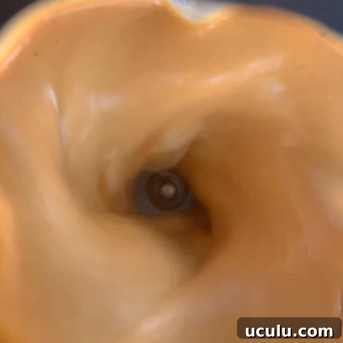 Close-up view of a creamy, light brown mixture being blended in a blender, with the blades visible at the center.