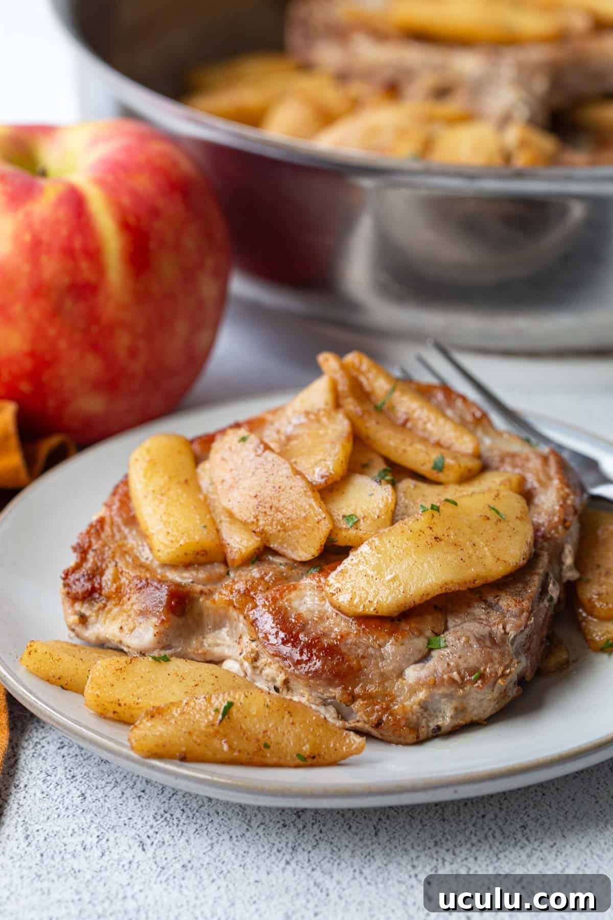 plate with a pork chop topped with apples.