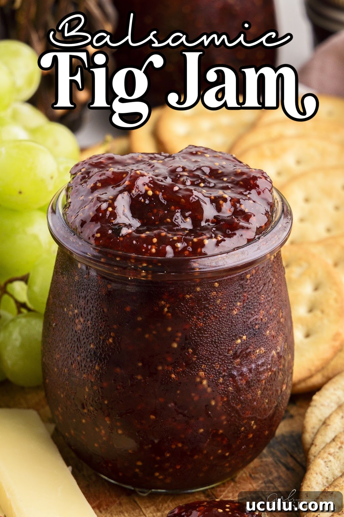 Glass jar filled with homemade balsamic fig jam with crackers, cheese, and fresh fruit placed around.