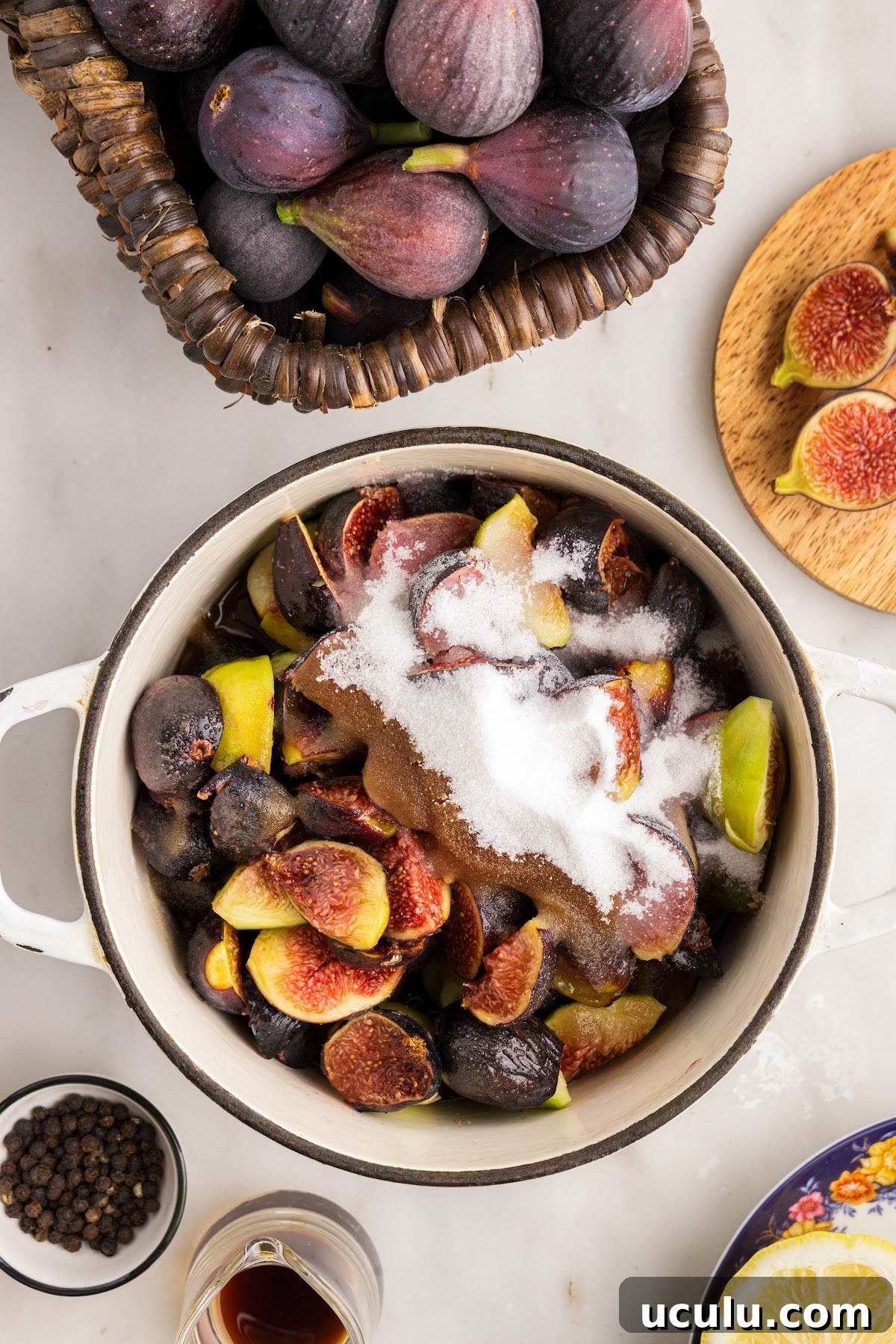 Saucepan with fresh cut figs and sugar, balsamic vinegar, and lemon juice. Fresh ingredients for this jam recipe in the background.