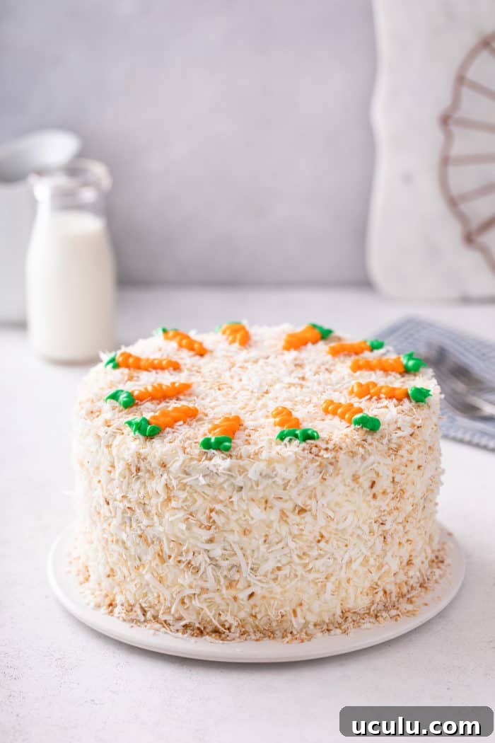 Assembled carrot cake, coated with toasted coconut and decorated with icing carrots on the top.
