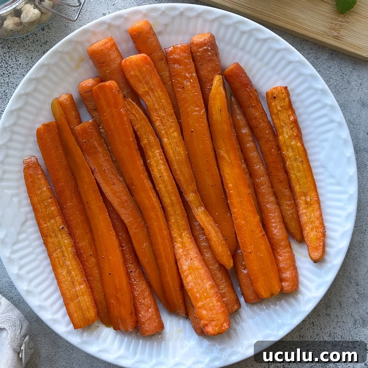 A white plate filled with Roasted Maple Carrots, lightly seasoned and arranged in a single layer on a gray surface.