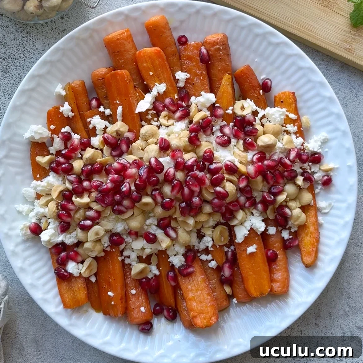 Roasted Maple Carrots on a white plate topped with crumbled feta, pomegranate seeds, and chopped hazelnuts.