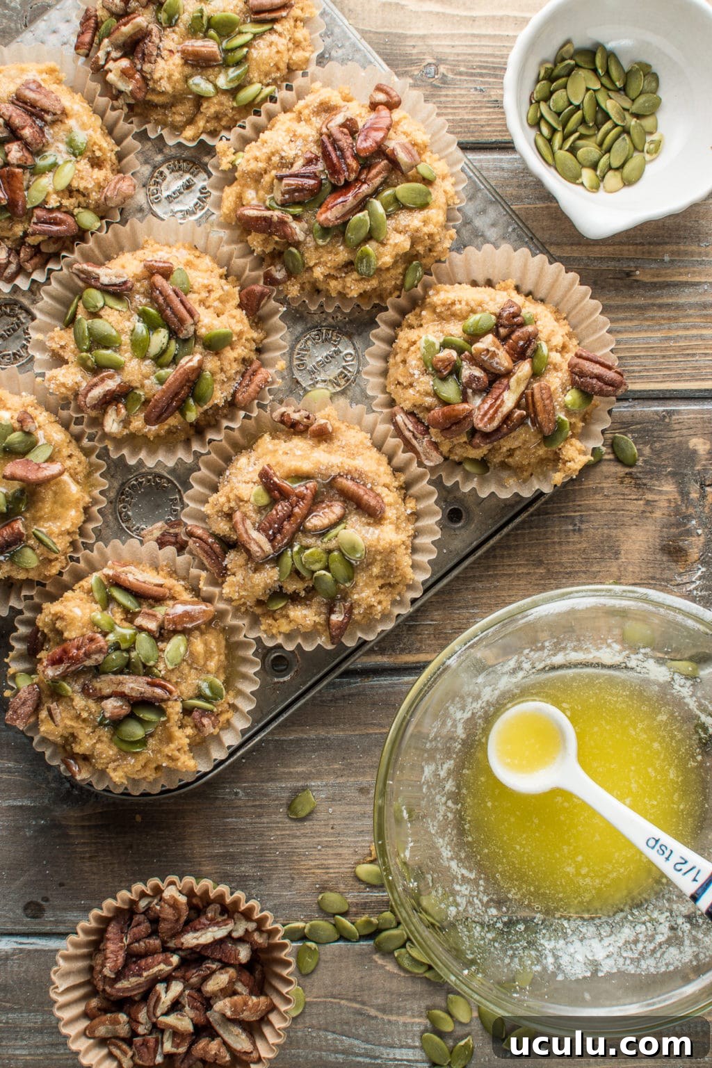 Muffin liners in a baking tray, filled with batter and topped with nuts.