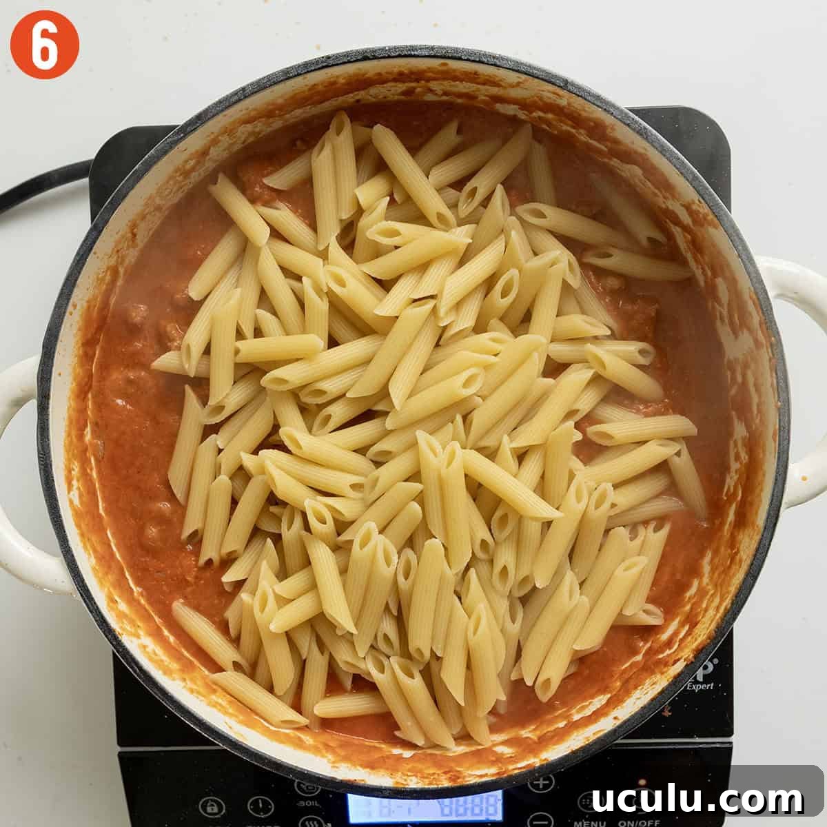 Adding pasta to the pink sauce.
