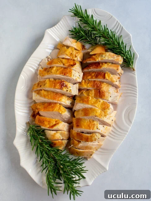 Sliced turkey breast on a white platter with fresh rosemary.