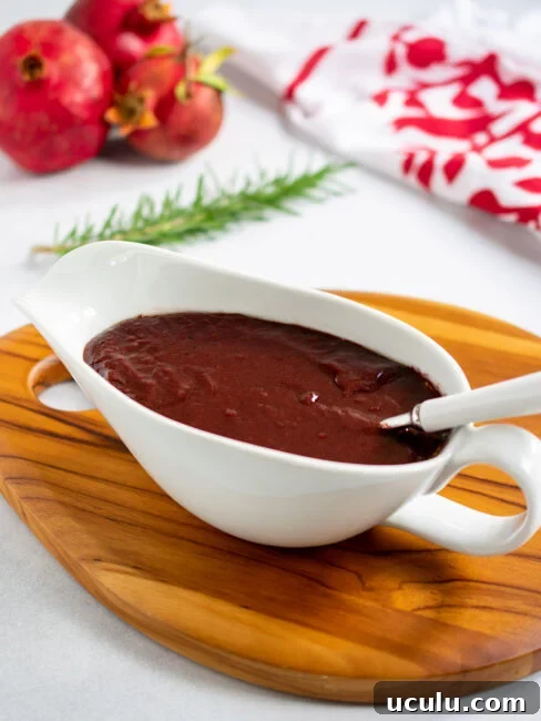 Pomegranate gravy in a white gravy boat with a white handled spoon with pomegranates in the background.