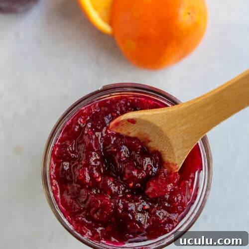 Cranberry orange jam in a jar with a wooden spoon inside.
