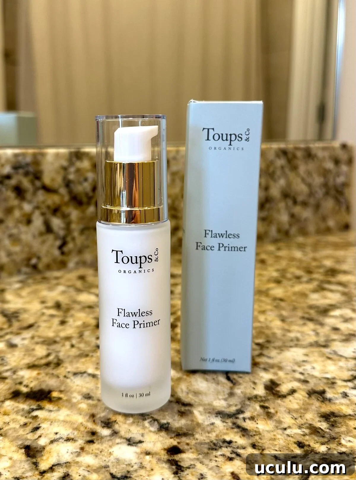 Bottle of Toups & Co Flawless Face Primer standing next to its box on a granite countertop.