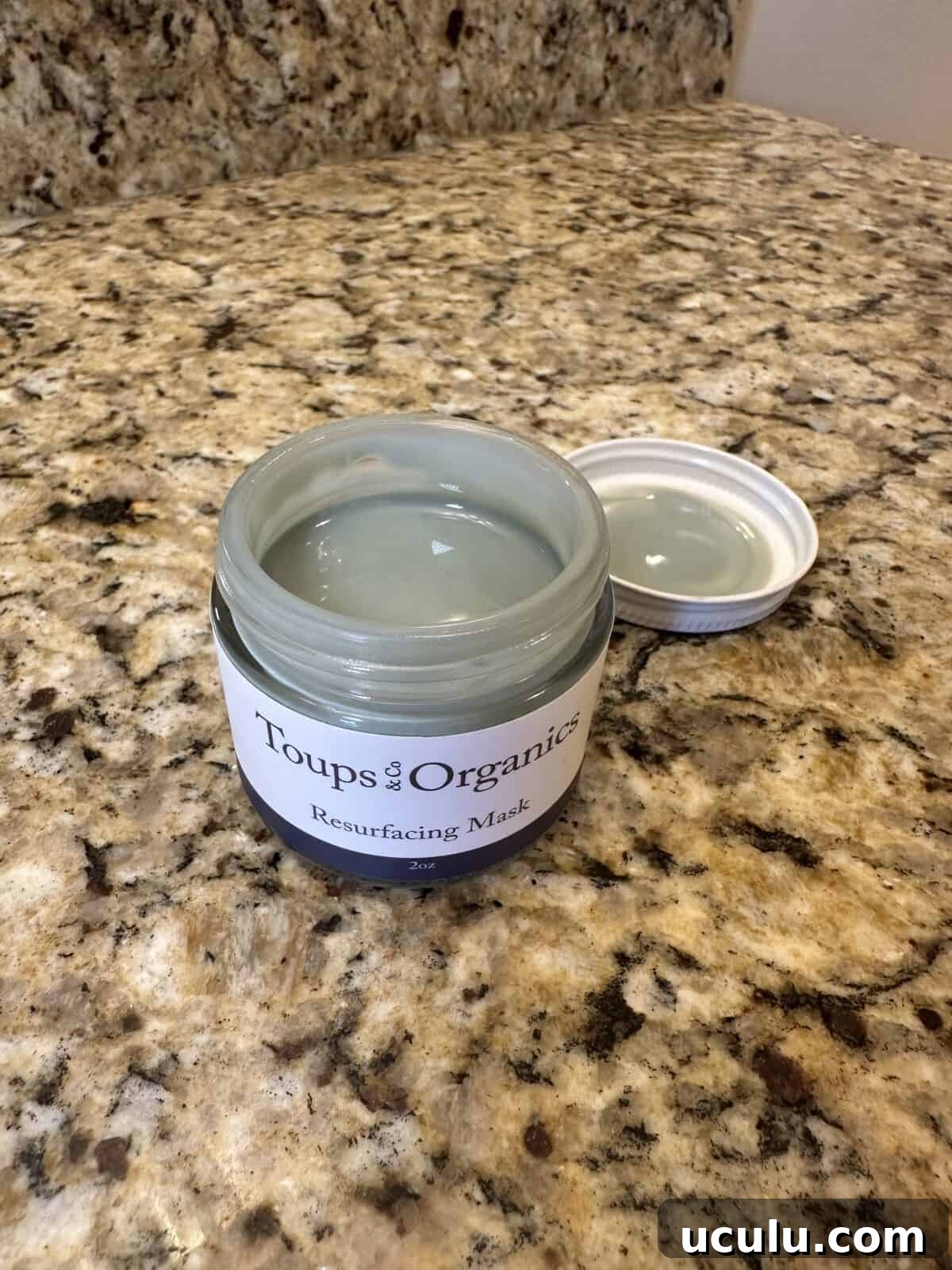 Open jar of Toups & Co Organics Resurfacing Mask on a granite countertop, with lid placed beside it.