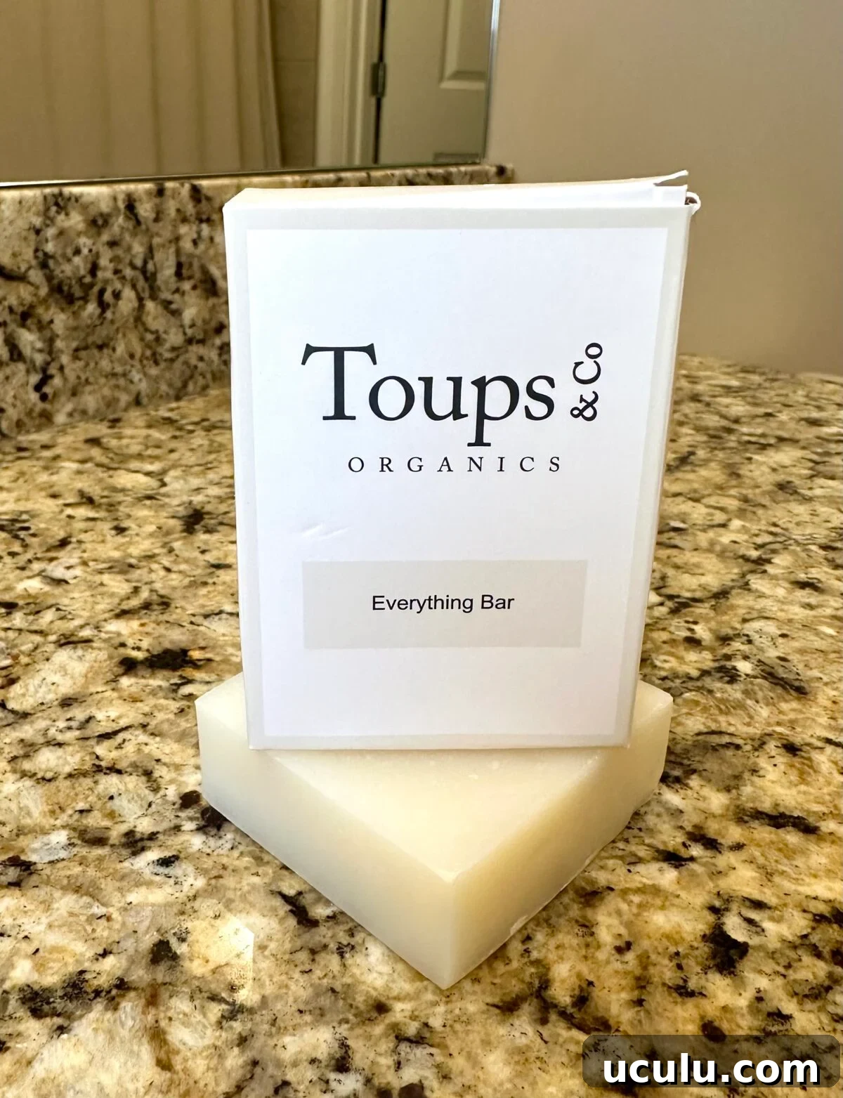 Toups & Co Organics Everything Bar soap displayed on a granite bathroom counter with its white packaging behind it.