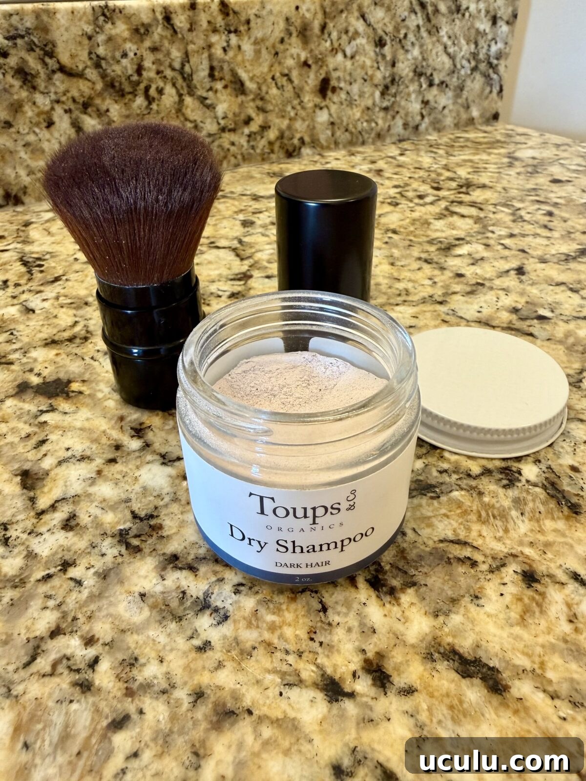 A jar of Toups & Co Organics Dry Shampoo for dark hair sits open on a granite countertop.