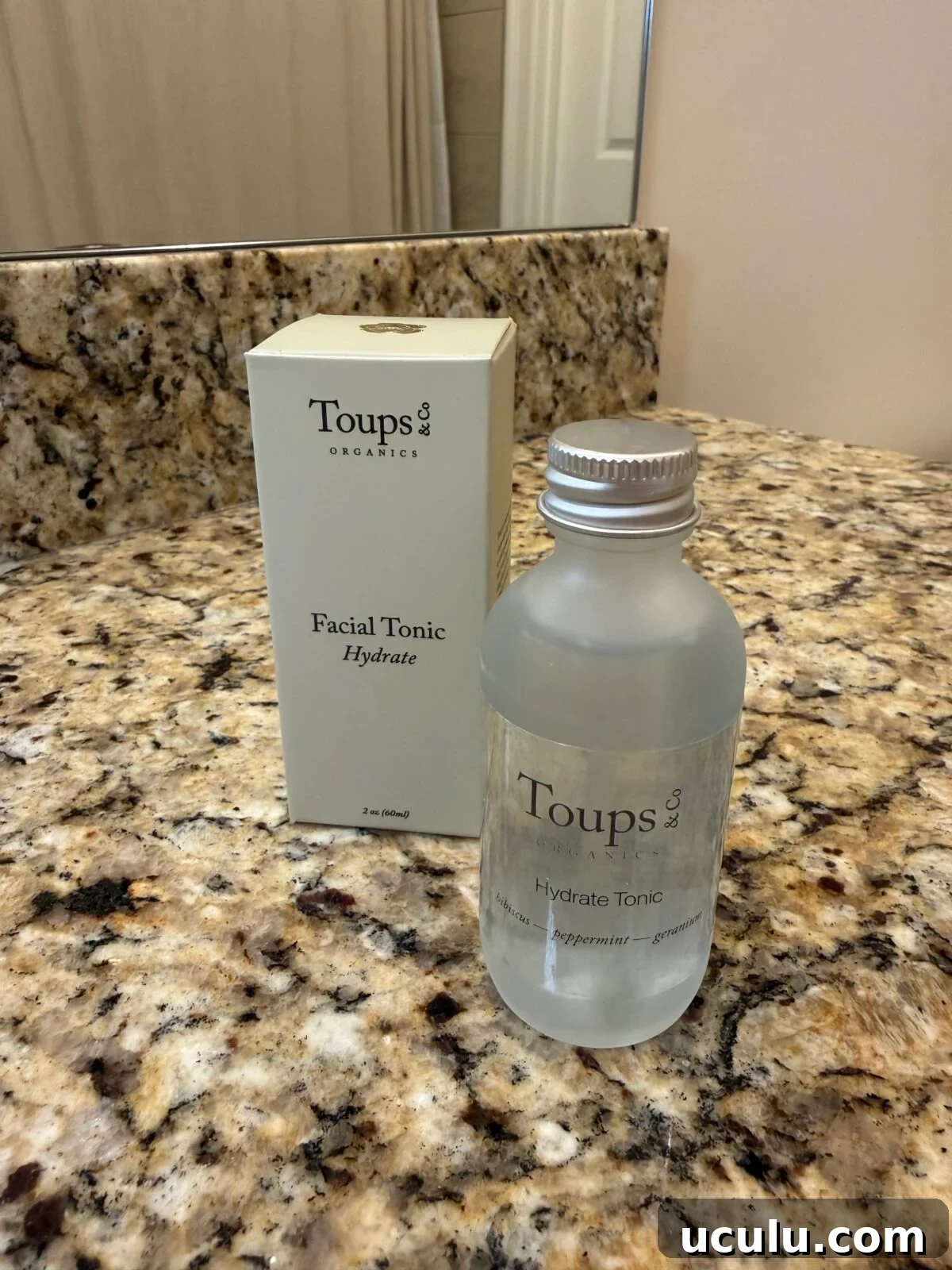 Toups & Co Organics Hydrate Facial Tonic bottle with aluminum cap and box, 2 oz, with hibiscus, peppermint, and geranium, on granite bathroom counter