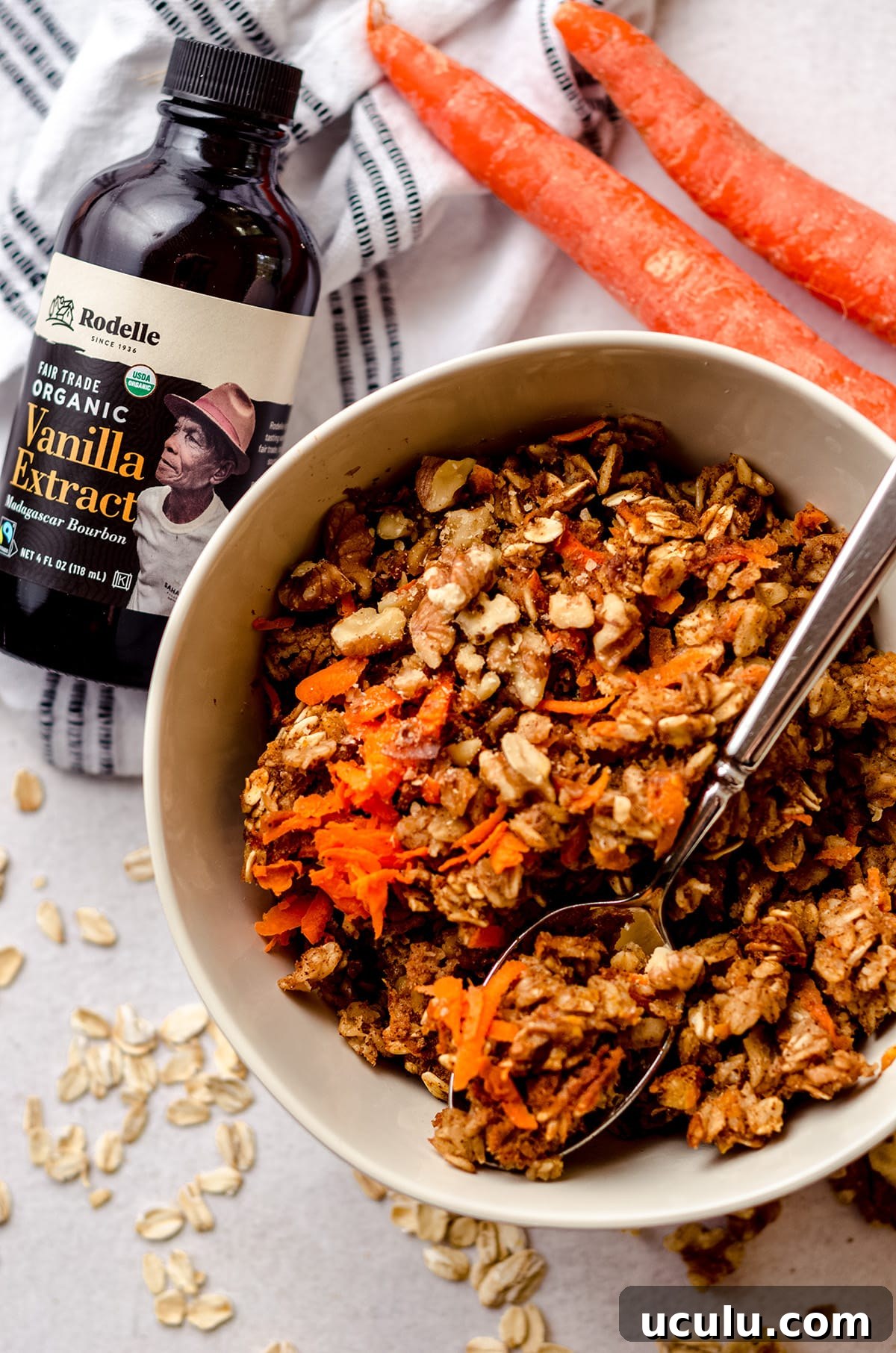 carrot cake baked oatmeal in a bowl with a spoon and a bottle of vanilla extract in the background