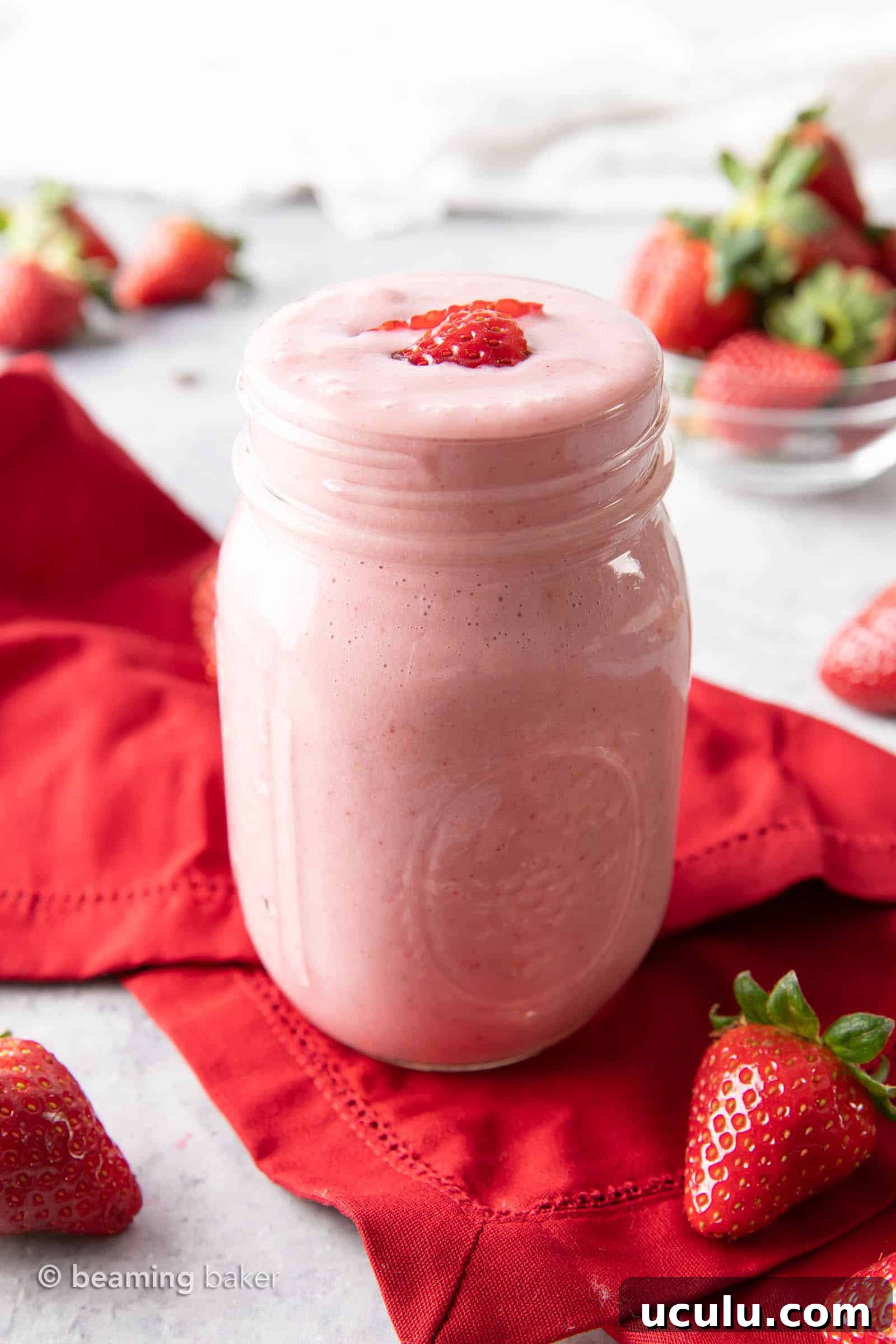 mason jar filled with strawberry protein shake on a red napkin, with strawberry slices on top.