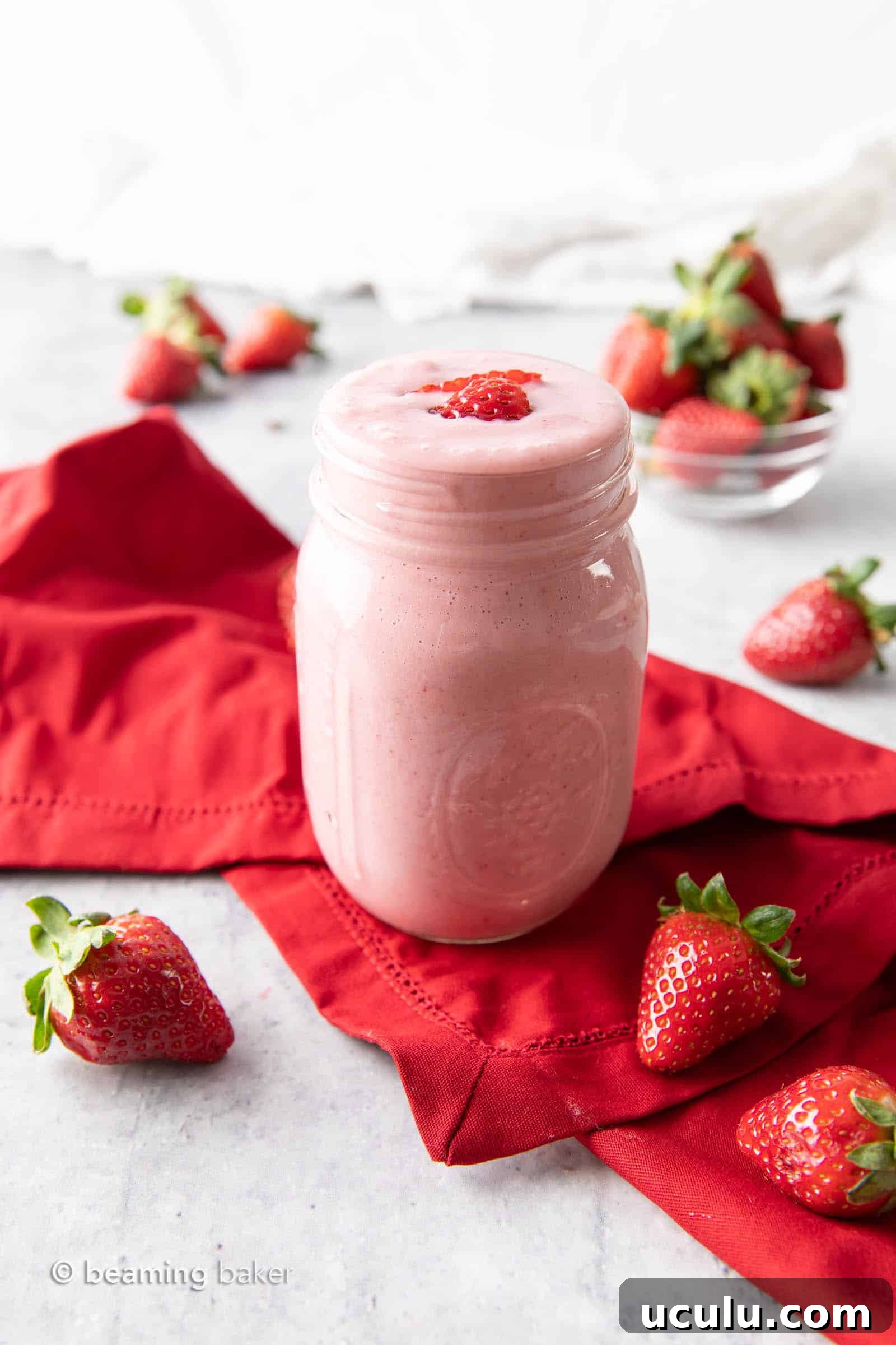 Glass of protein shake on a red napkin with strawberries on counter and in bowl.