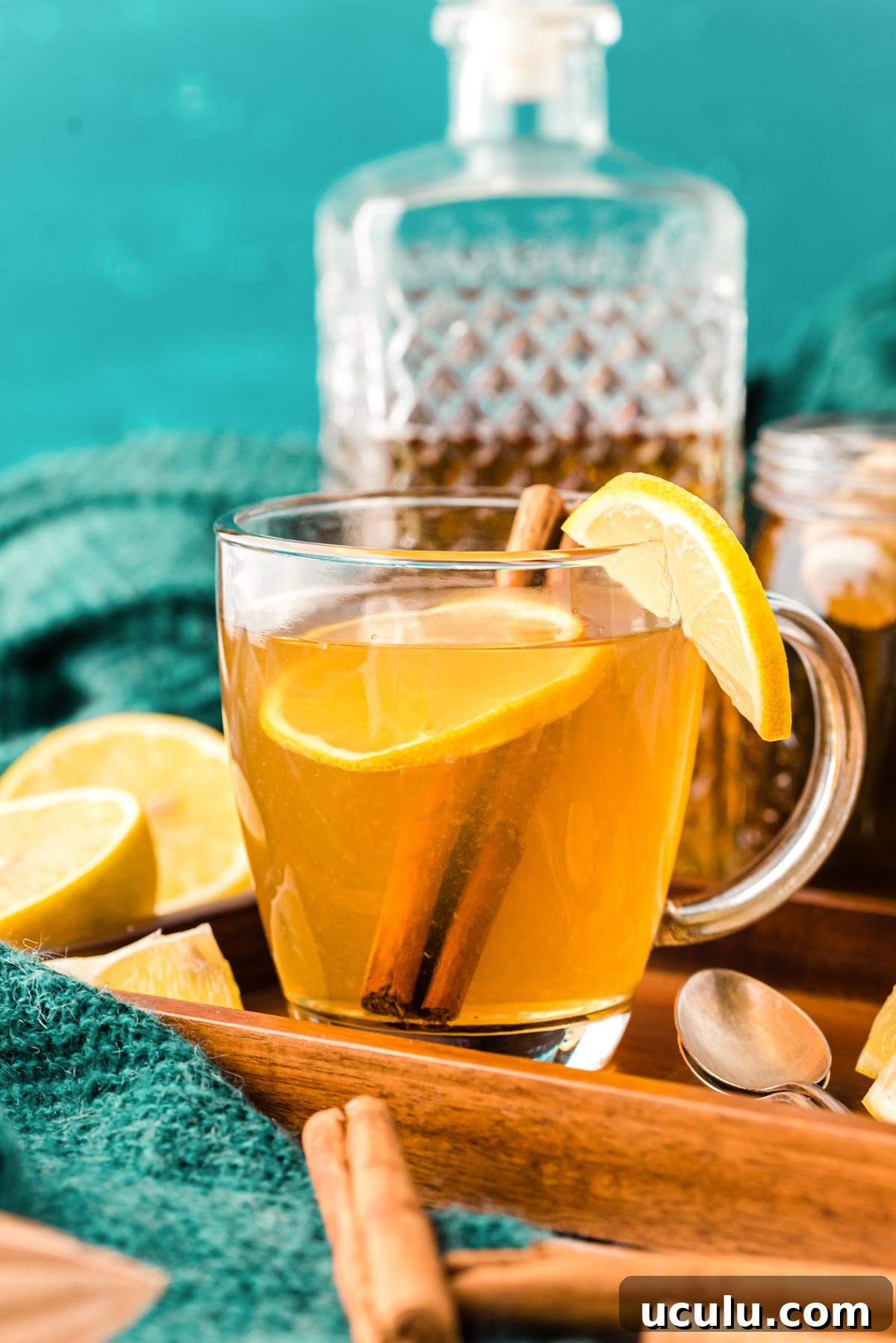 A hot toddy garnished with lemon in a clear glass mug on a wooden tray.