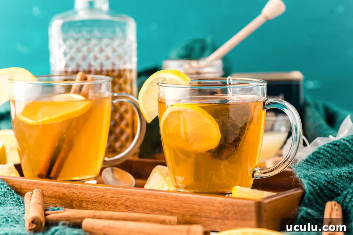 2 mugs on a wooden tray filling with tea, lemon, honey, and whiskey.